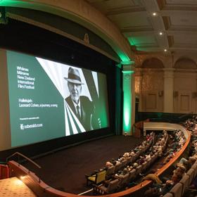 Inside a theatre at Embassy Cinemas, located in Te Aro, Wellington. There are vaulted ceilings, pillars and most of the seats are occupied by audience members. 'Whānau Mārama: New Zealand International Film Festiva' is projected on the large screen.