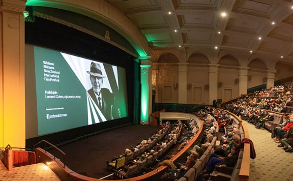 Inside a theatre at Embassy Cinemas, located in Te Aro, Wellington. There are vaulted ceilings, pillars and most of the seats are occupied by audience members. 'Whānau Mārama: New Zealand International Film Festiva' is projected on the large screen.