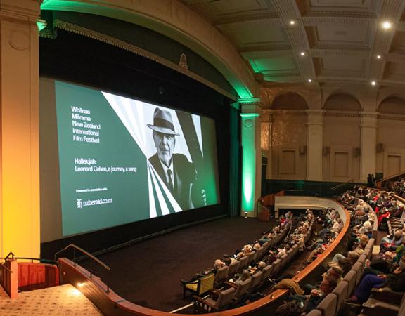 Inside a theatre at Embassy Cinemas, located in Te Aro, Wellington. There are vaulted ceilings, pillars and most of the seats are occupied by audience members. 'Whānau Mārama: New Zealand International Film Festiva' is projected on the large screen.