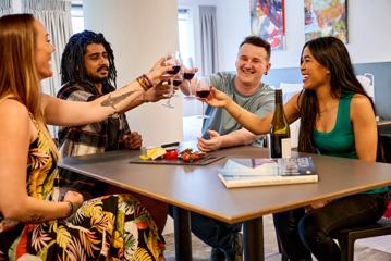 Four people are sitting together around a table, raising glasses of red wine at the Sojurn Apartment Hotel in Wellington, New Zealand.