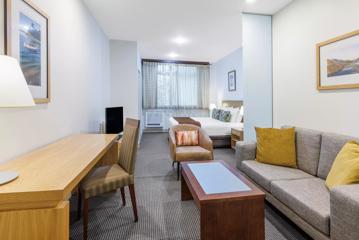 The long CityLife Hotel room has a bed in the background under a window, with a desk, couch, and coffee table in the foreground.