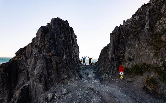 Two people stand with their arms raised at Devil's Gate on the Red Rocks Coastal Walkway in Ōwhiro Bay in Wellington.