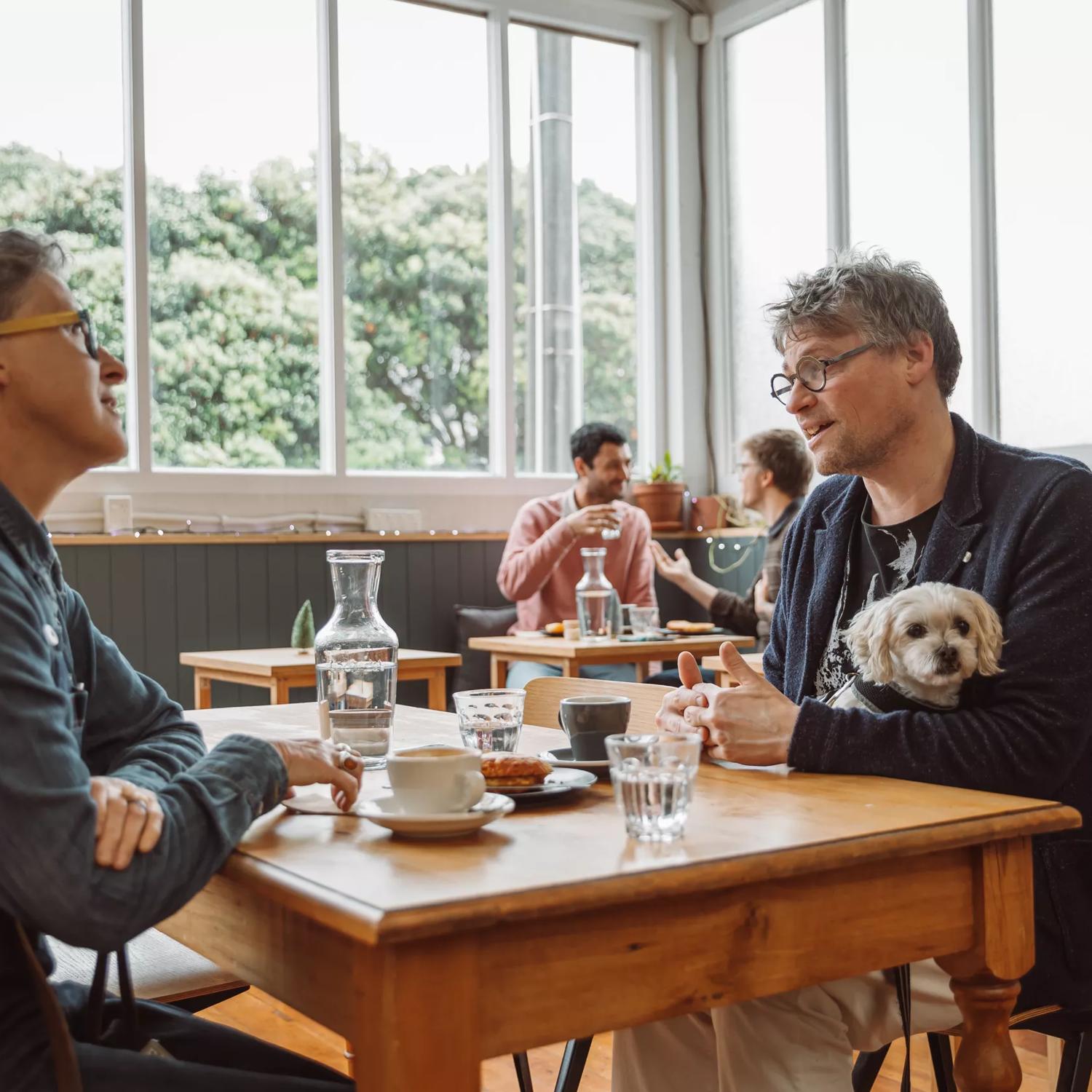 Two people sit at a table drinking coffee and eating a pastry at People Coffee Roastery in Newtown, Wellington. 