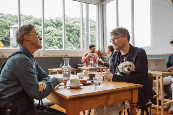 Two people sit at a table drinking coffee and eating a pastry at People Coffee Roastery in Newtown, Wellington. 