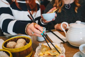 A person with teal-painted fingernails uses chopsticks to pick up a gyoza.