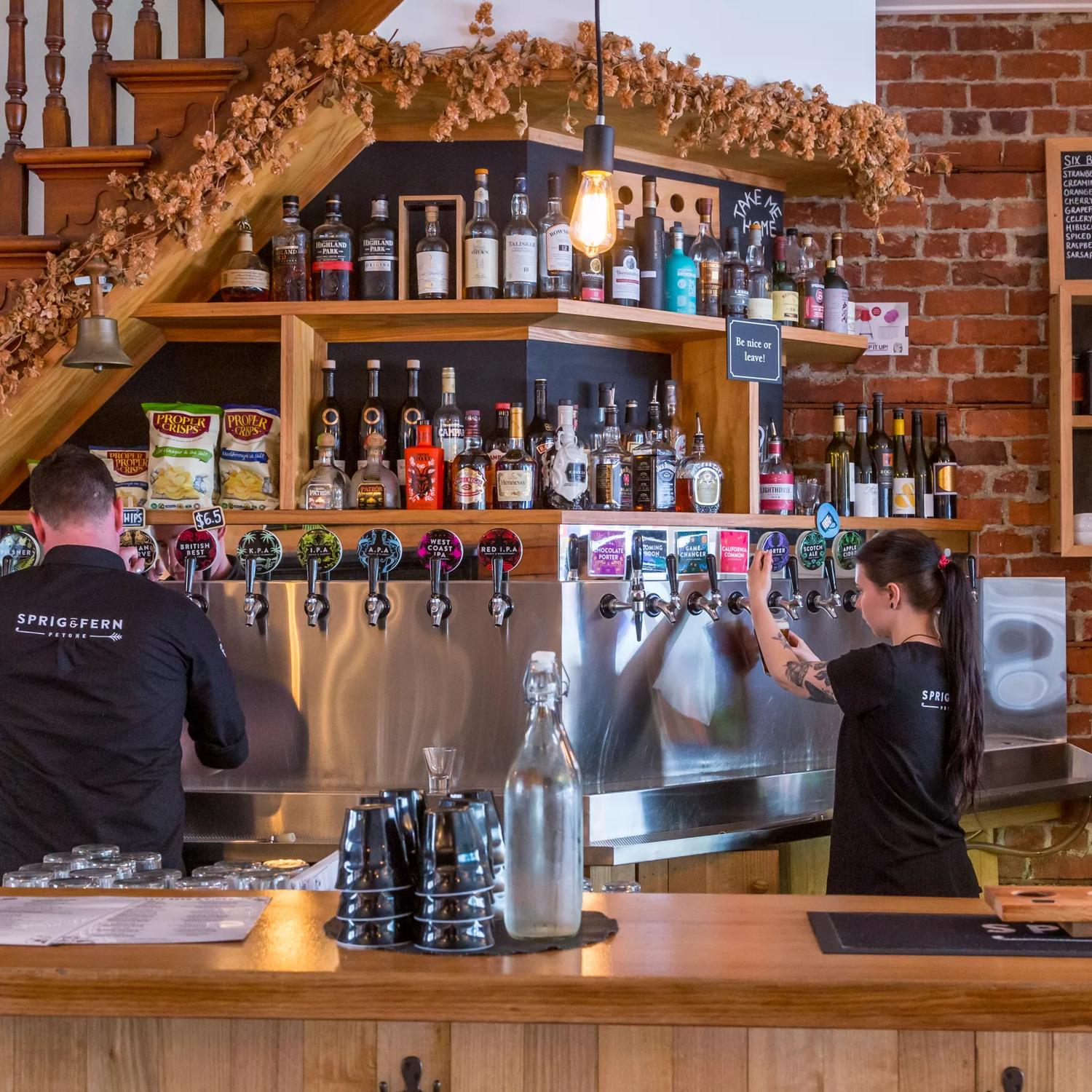 The bar at Sprig + Fern Tavern in Petone, Lower Hutt. Two workers are pouring draught beers. 