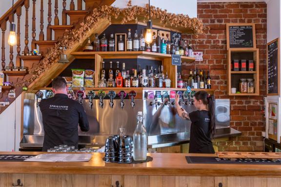 The bar at Sprig + Fern Tavern in Petone, Lower Hutt. Two workers are pouring draught beers. 