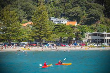 Kayakers in the blue water of Days Bay while beach-goers enjoy the sun on the shore.