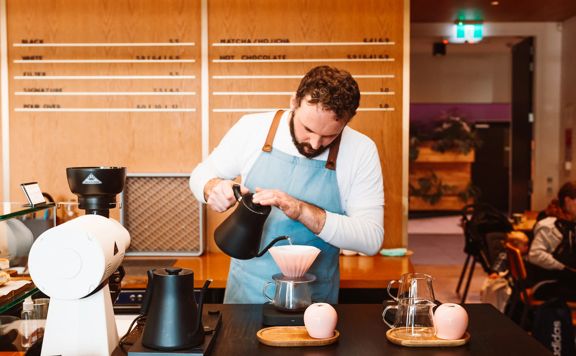 A barista in a blue apron prepares pour-over coffee.