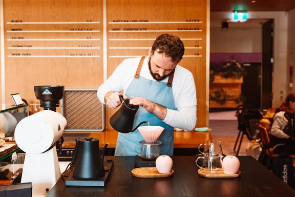 A barista in a blue apron prepares pour-over coffee.
