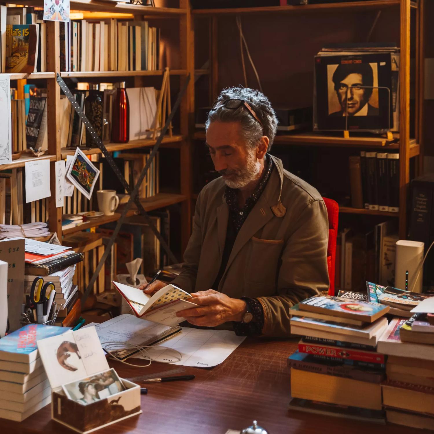 A person sits behind a desk looking at a book, while surrounded by piles and shelves of books in The Undercurrent bookstore.