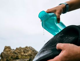 Water pours from a bright blue bottle onto a wetsuit.