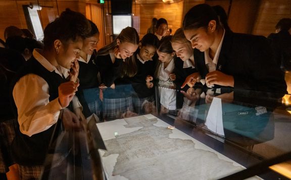 Visitors gather around a display case viewing Te Tiriti o Waitangi at He Tohu in the National Library of New Zealand.