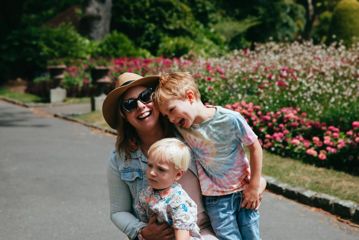 An adult and two kids hug and laugh on a path lined with flowers at Wellington Botanic Garden.