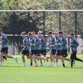 The Wellington Phoenix men's football team runs together on a football field. 