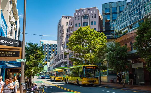 Wide of Bond Street in Wellington, with two yellow buses driving down the road.