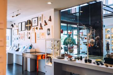 Inside a gift shop at an art museum. There are art pieces on the wall and small trinkets for sale on a row of tables.