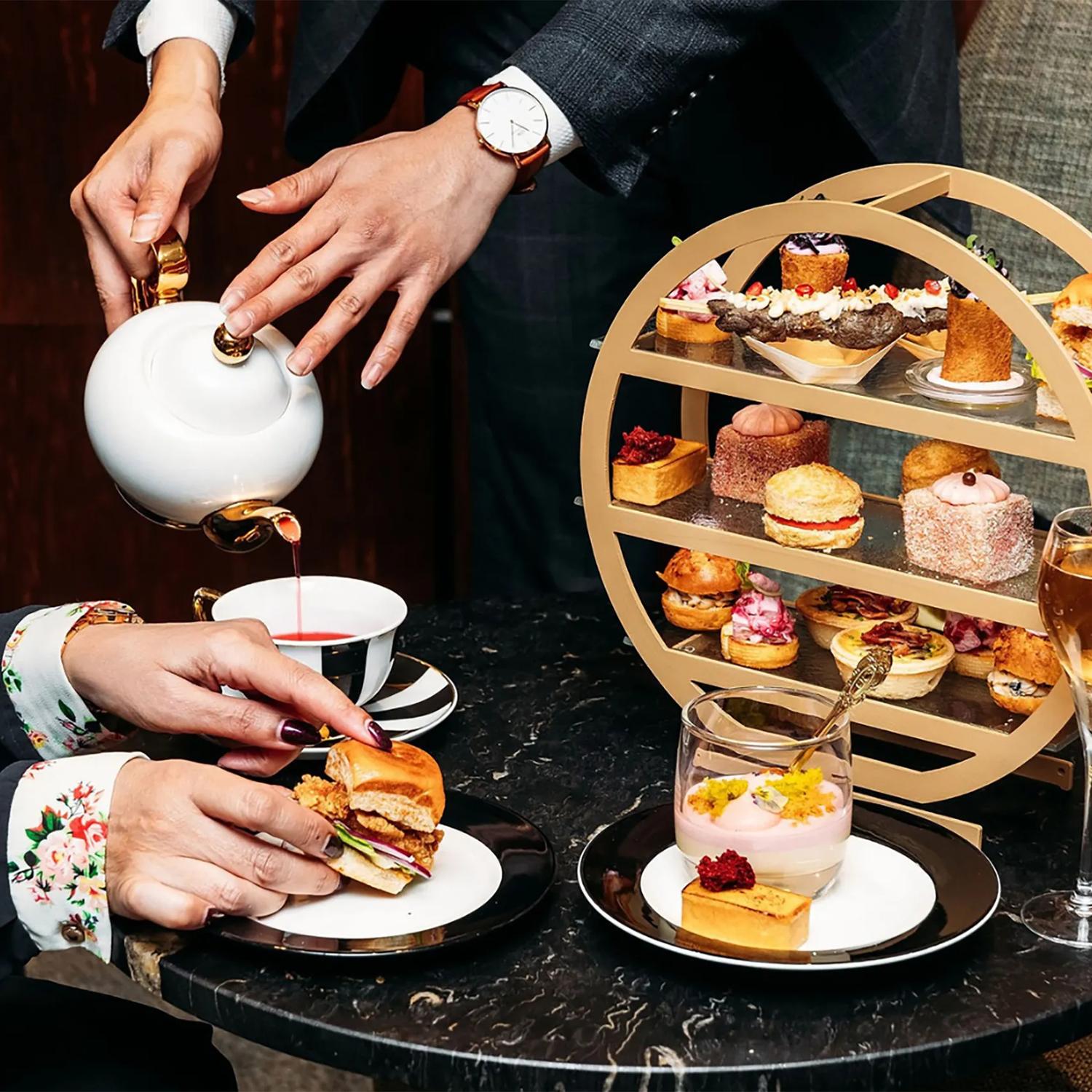 A High Tea spread at InterContinental Lobby Lounge in Wellington. Tea is being poured and cute little snacks are arranged on a multi-tiered tray.