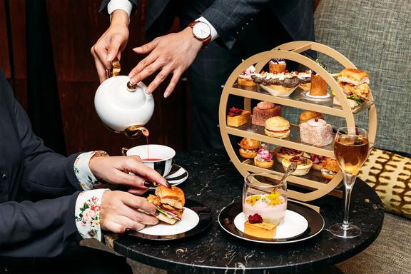 A High Tea spread at InterContinental Lobby Lounge in Wellington. Tea is being poured and cute little snacks are arranged on a multi-tiered tray.