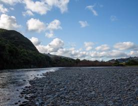 The Taitā Rock swimming hole in Lower Hutt, with lush green bush surrounding a blue river and large pebbles on the shore.