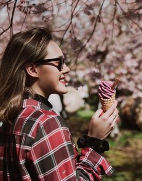 A person wearing sunglasses holding an ice cream, surrounded by cherry blossoms.