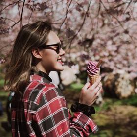A person wearing sunglasses holding an ice cream, surrounded by cherry blossoms.