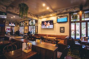 Interior of The Bridge bar at the Cambridge Hotel. There's café style tables and booth seating, with TVs on the walls.