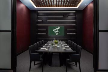 A dark modern boardroom with dark red walls, a large table with five leather chairs on either side, set up with water glasses, paper and pens.