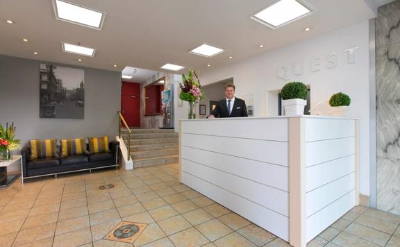 A concierge is standing behind the front desk at Quest on the Terrace, a four star hotel located in central Wellington.