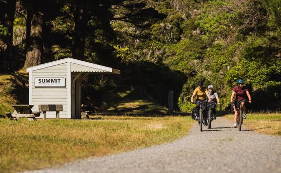 Three bikers on a gravel path at the summit building of the Remutaka Cycle trail.