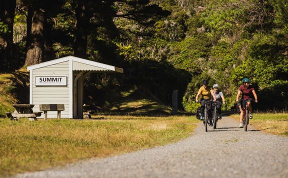 Three bikers on a gravel path at the summit building of the Remutaka Cycle trail.