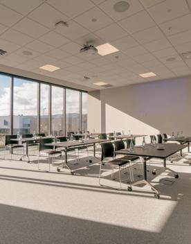 A smaller room inside Lower Hutt Events Centre, with 18 chairs at tables facing the front of the room. Behind them are very large glass windows looking out over Lower Hutt town centre.
