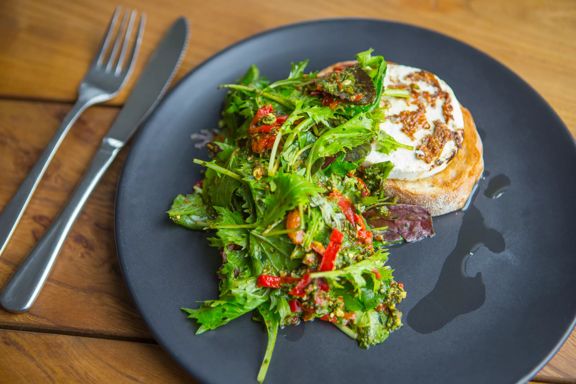 Fresh green salad with red chilies and a poached egg on toasted bread, served on a dark plate with fork and knife.