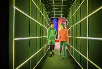 2 children walking through a tunnel at Space place lit up by green LED lights.