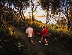 Two people walk along Bus Barn Track in East Harbour Regional Park during golden hour.