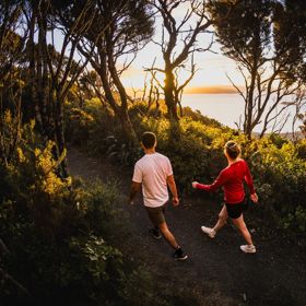 Two people walk along Bus Barn Track in East Harbour Regional Park during golden hour.