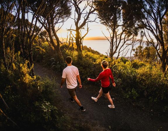 Two people walk along Bus Barn Track in East Harbour Regional Park during golden hour.