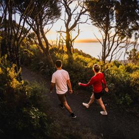 Two people walk along Bus Barn Track in East Harbour Regional Park during golden hour.