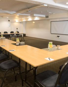 A business venue inside West Plaza Hotel with a large u shaped table set up and 20 chairs facing a whiteboard.