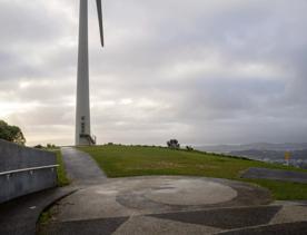 The Brooklyn Wind Turbine sits on a hill above Wellington, with views of the city. Bush and trees surround the area.