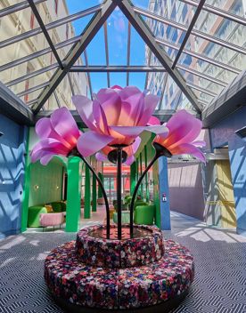 Inside the foyer of Naumi Studio Wellington, where a large pink flower statue sits on top of an upholstered circular seat with flower designs. The room is all glass, the walls are blue, and the floor is a geometric pattern.