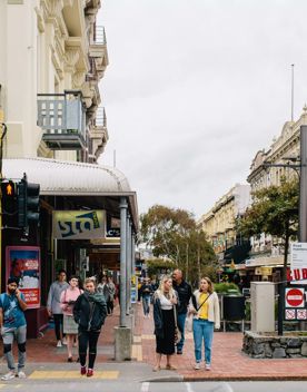 The corner of Cuba Street at Ghuznee Street, with pedestrians waiting to cross the road, on a cloudy day.