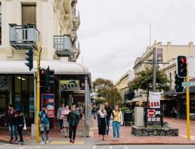 The corner of Cuba Street at Ghuznee Street, with pedestrians waiting to cross the road, on a cloudy day.