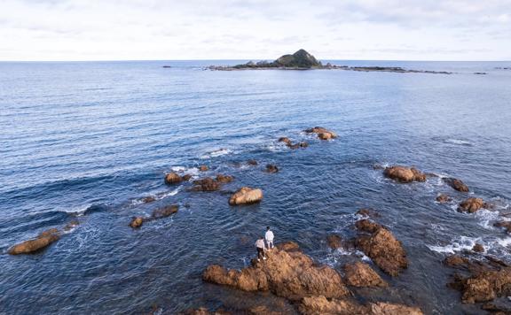 Two people stand on the rocky shoreline on the Southern Walkway in Wellington. 