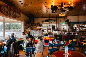 Customers sitting inside Maranui Cafe enjoying the lookout over Lyall Bay and their meals. Fish and surf decor surround the room.
