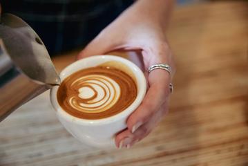 A hand holding a coffee cup creating latte art at Swimsuit Café in Wellington, New Zealand.