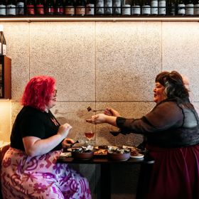 Two people at Rosella eating food. A rack of wine bottles is above them.