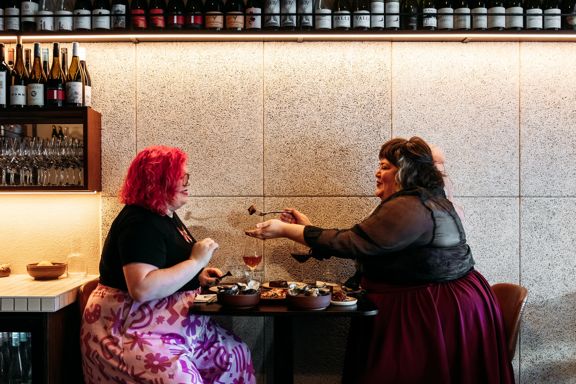 Two people at Rosella eating food. A rack of wine bottles is above them.