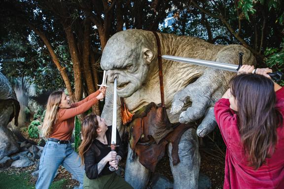 3 people outside Wētā workshops, poking swords at a hill troll from Lord of the Rings.