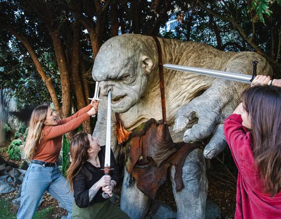 3 people outside Wētā workshops, poking swords at a hill troll from Lord of the Rings.
